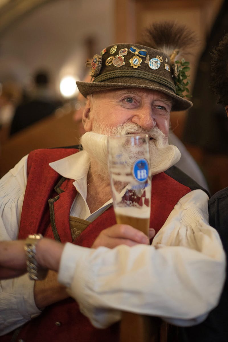 Senior man with hat and gray beard holding a beer glass at Oktoberfest in Munich, Germany.