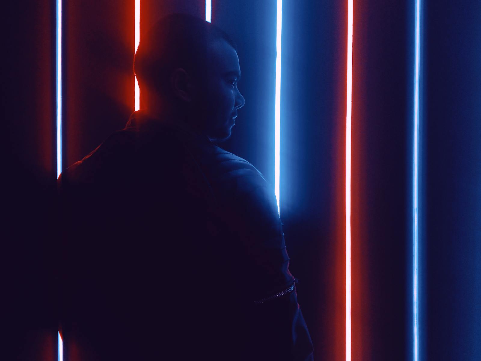 A man stands against a backdrop of blue and red neon lights, creating a striking silhouette.