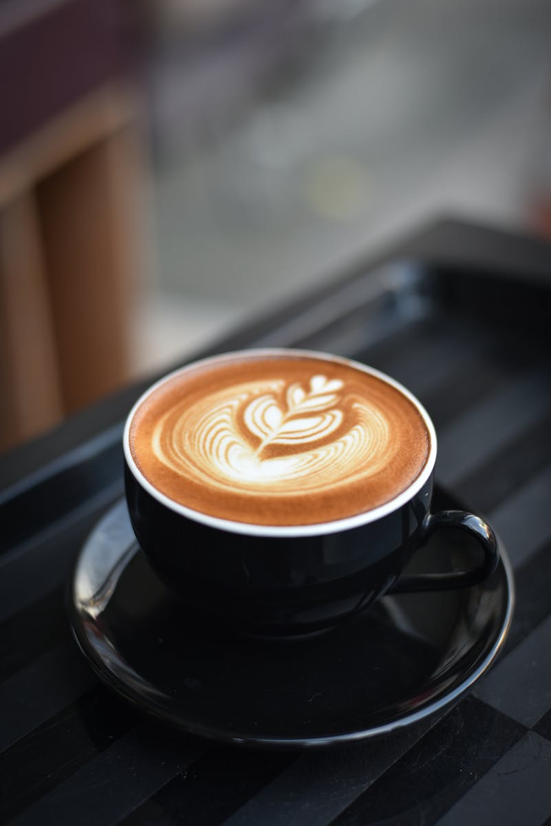 A beautifully crafted cappuccino with intricate latte art in a black ceramic mug on a dark surface.