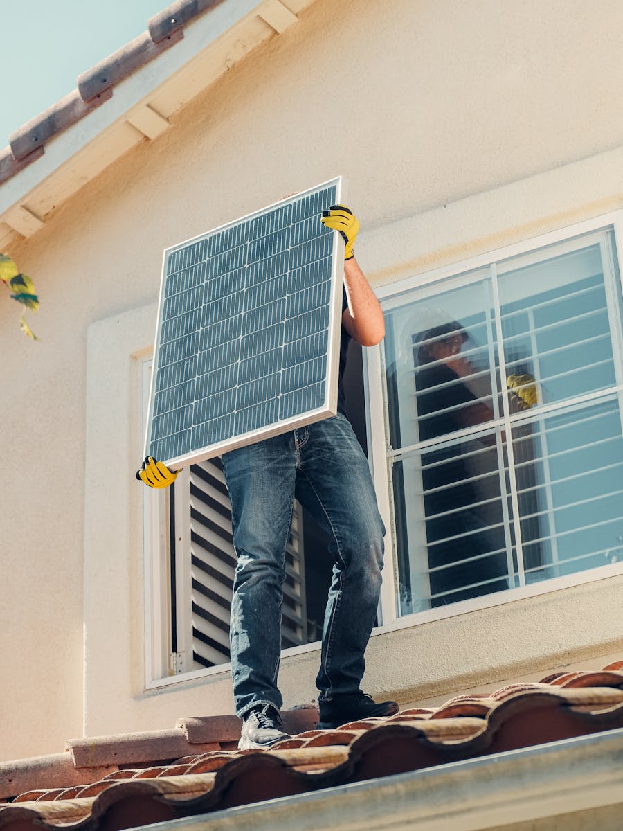 Technician carrying a solar panel on a rooftop for installation, promoting renewable energy.